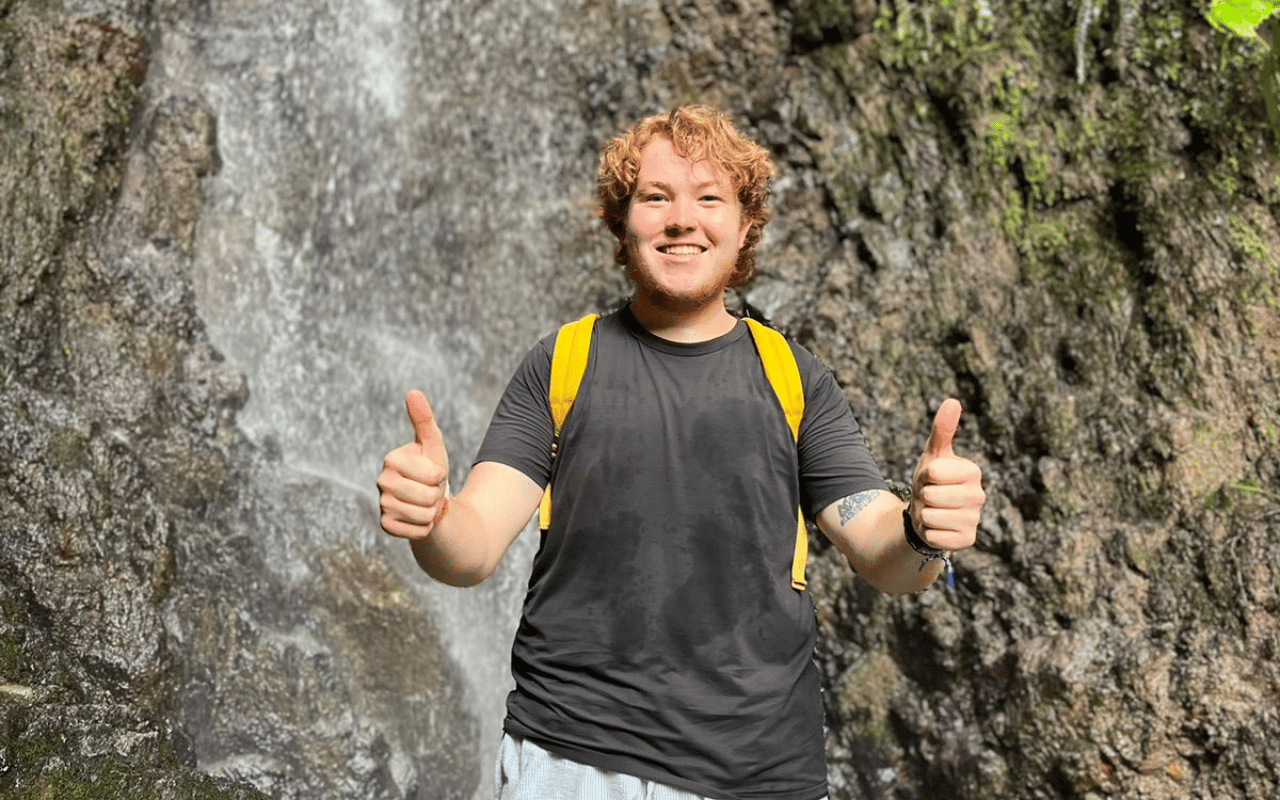 A picture of Birkley Heynen giving a thumbs-up in front of a waterfall.